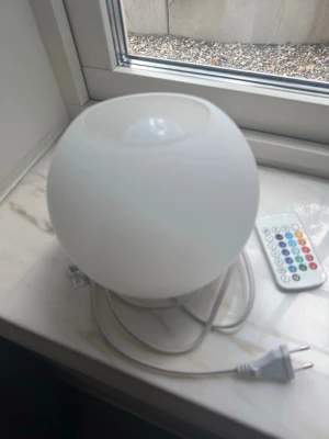 Vit rund bordslampa med fjärrkontroll - Säljer en vit, rund bordslampa i glas med sladd och stickkontakt. Lampan styrs med en medföljande fjärrkontroll som har flera färgval och ljusinställningar. Perfekt som mysbelysning eller dekoration i rummet.