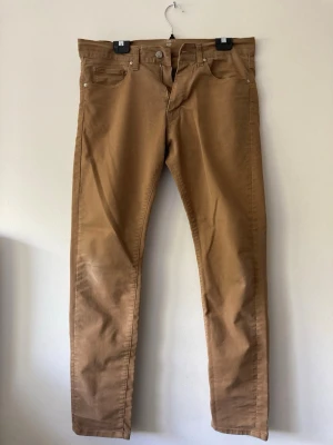 Beiga chinos med rak passform - Snygga beiga chinos med klassisk rak passform och fem fickor. Byxorna har bälteshällor och stängs med knapp och dragkedja. Perfekta för en stilren och avslappnad look. Tillverkade i mjukt bomullstyg som känns skönt mot huden.