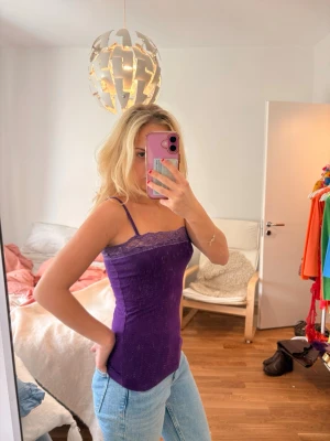 Lila linnetopp med spetsdetalj - Snygg lila linnetopp med smala axelband och spets upptill. Toppen har en tight passform och är perfekt att styla med jeans eller kjol. Materialet känns mjukt och stretchigt, vilket gör den bekväm att bära hela dagen. Köpt i Bangkok (klippt av taggen men märket är originalet Kv shop)
