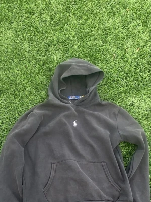Svart hoodie från Polo Ralph Lauren - Svart hoodie från Polo Ralph Lauren med klassisk huva och känguruficka. Ikoniska vita Polo-loggan broderad på bröstet. Tillverkad i mjukt bomullsmaterial som är skönt att bära. Perfekt för en avslappnad och stilren look.