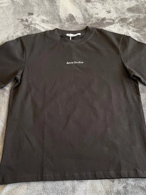 Svart Acne Studios t-shirt - Snygg svart t-shirt från Acne Studios med minimalistisk logga tryckt på bröstet. Klassisk rund halsringning och korta ärmar. Perfekt basplagg i mjuk bomull som funkar till allt.