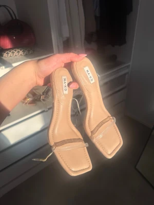 Beige sandaler med transparent rem NA-KD - Snygga sandaler från NA-KD i beige med fyrkantig tå och transparenta remmar. Klack och stilren design som passar perfekt till sommarens outfits. Tillverkade i syntetmaterial med modern look.