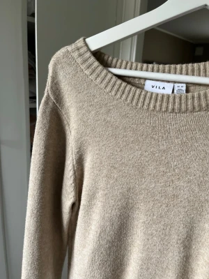 Beige stickad tröja från Vila - Beige stickad tröja från Vila med rund halsringning och ribbade muddar. Tröjan har en enkel och stilren design, perfekt för lager-på-lager och passar till många olika outfits. Mjuk och skön kvalitet.