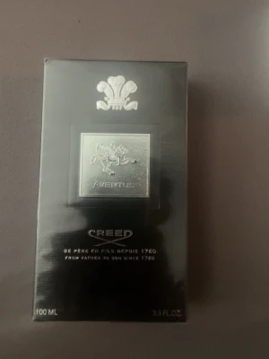 Creed Aventus Eau de Parfum 100ml - Lyxig parfym från Creed, Aventus, i en elegant svart och silverfärgad förpackning. Flaskan rymmer 100 ml och har exklusiva detaljer med en silveremblem och klassisk design. Perfekt för dig som gillar sofistikerade och tidlösa dofter.