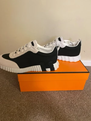 H märkes skor - Snygga sneakers från H i svart och vitt med coola detaljer och vågig sula. Ovandelen är i textil och läder, med vita skosnören och orange detalj på sulan. Perfekta för dig som vill sticka ut med stilrena och trendiga skor.