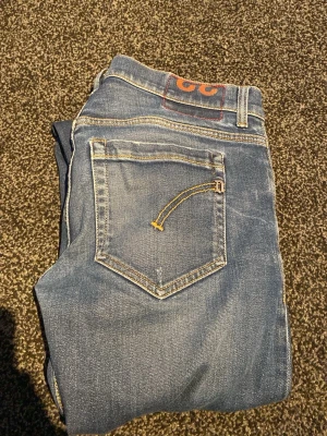 Dondup george  - Snygga blå jeans med smal passform och klassiska kontrastsömmar. Jeansen har två bakfickor med dekorativa gula sömmar och en patch med siffror på linningen. Perfekta för en avslappnad och trendig look.