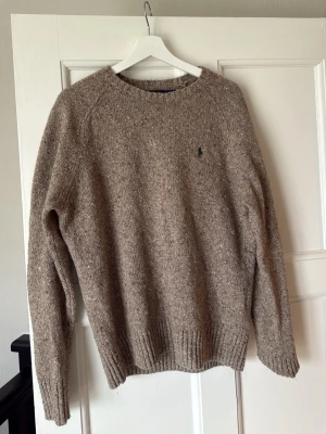 Beige stickad tröja från Ralph Lauren - Klassisk beige stickad tröja från Ralph Lauren med rund halsringning och diskret broderad logga på bröstet. 