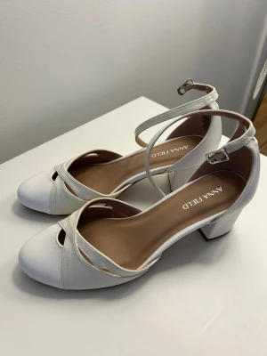 Vita sandaler med remmar från Anna Field - Snygga vita sandaler från Anna Field med rund tå, bred klack och eleganta korsade remmar över foten. Skorna har justerbar ankelrem med spänne och är tillverkade i ett slätt material som ger en stilren look. Perfekta för att lyfta din outfit. Aldrig använda 