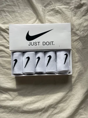 Vita Nike strumpor i 5-pack - Säljer ett 5-pack vita Nike strumpor med svart logga. Strumporna är ribbade och har klassisk sportig design. Perfekta för dig som gillar stilrena och bekväma strumpor med ikonisk Nike Swoosh. Kommer i originalförpackning.
