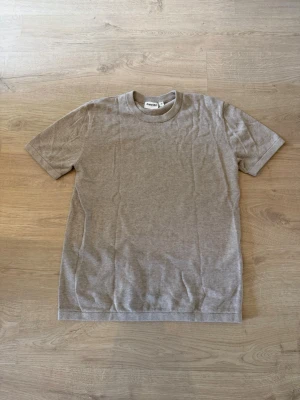 Biege stickad t-shirt - En enkel och stilren biege t-shirt. T-shirten har rund halsringning och korta ärmar. Stickad för en bekväm känsla. Perfekt att matcha med jeans eller shorts.