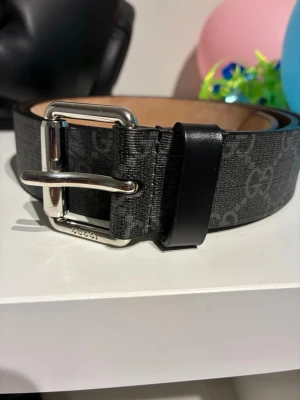 Gucci svart bälte med orm-motiv - Snyggt svart bälte från Gucci med silverfärgat spänne och ikoniskt GG-mönster. Bältet har ett coolt orm-motiv i rött och vitt. Tillverkat i skinn med detaljer i syntet. Perfekt accessoar för att lyfta din outfit.