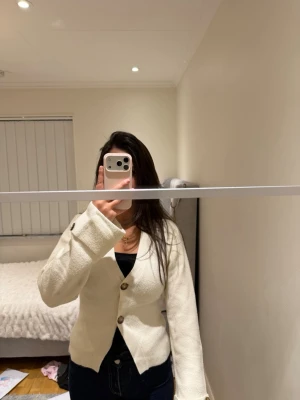 Vit kofta med knappar - Snygg vit kofta med stora bruna knappar framtill. Koftan har en rak passform, långa ärmar och är tillverkad i ett mjukt material. Perfekt att slänga över en topp för en clean look.