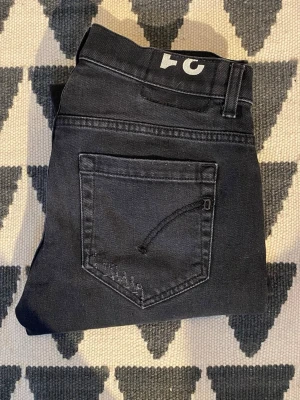 Svarta dondups - Snygga svarta jeans med rak passform och klassiska fem fickor. Jeansen har en diskret tvättad look och bälteshällor. Perfekta för en stilren och avslappnad outfit.