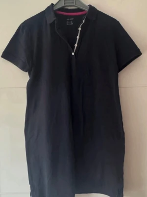 Marinblått kortärmad skjortklänning - En enkel och stilren skjortklänning med korta ärmar och krage. Klänningen har knappar framtill och en rak passform som ger en avslappnad look. Perfekt för varma dagar och lätt att matcha med accessoarer.