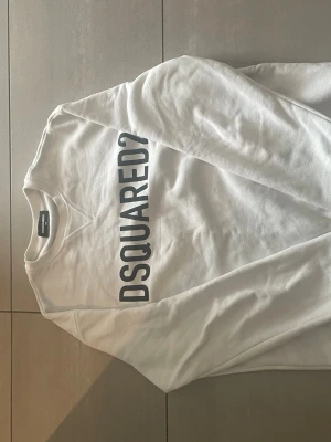Vit sweatshirt från Dsquared2 - Snygg vit sweatshirt från Dsquared2 med stor svart logga tryckt diagonalt över framsidan. Tröjan har rund halsringning och är tillverkad i mjukt material, perfekt för en avslappnad och trendig look. 