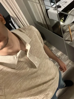 Beige kortärmad polotopp från H&M - Snygg beige polotopp från H&M med korta ärmar och klassisk krage. Toppen har knappar framtill och är tillverkad i mjuk bomullsmix. Perfekt för en avslappnad och stilren look.