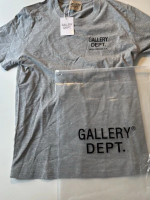 Grå t-shirt från Gallery Dept. - Snygg grå t-shirt från Gallery Dept. med svart tryck både fram och bak. Klassisk passform med rund hals skick 10/10 helt ny  den är i storlek S men passar även M den skickas samma dag som köp!