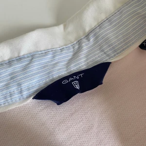 Pikétröja från Gant (äkta såklart) - Säljer min superfina pikétröja från Gant. Har växt ur den och den kom aldrig riktigt till användning. Behövs strykas men annars i fint skick! ”Hängare” på ryggen samt fina blårandiga detaljer här och där.