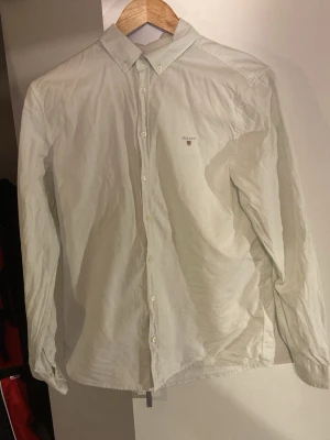 Vit skjorta från Gant med knappar - Klassisk vit skjorta från Gant med knappar hela vägen framtill och button-down krage. Skjortan har lång ärm och diskret Gant-logga broderad på bröstet. Perfekt för en clean och stilren look.