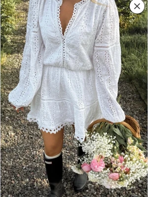 Vit broderad kort klänning - Söt vit kort klänning med broderade detaljer och volangkant. Klänningen har långärmade ärmar. Resår i midjan. Från Nelly, nypris ca 600kr. Använd två gånger.🥰