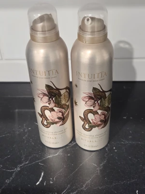Rituals Intuita Shower foam - Två flaskor Rituals Intuita foaming shower gel med elegant beige metallfinish och blommigt ormmotiv. Flaskorna har genomskinliga plastlock och rymmer 200 ml vardera. Perfekt för dig som vill ha en lyxig duschupplevelse.