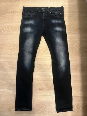Replay svarta slim fit jeans - Säljer ett par svarta slim fit jeans från Replay med snygga slitningar och tvättade detaljer på låren. Klassisk femficksmodell med metallknapp och dragkedja. Jeansen har en modern look och är tillverkade i stretchigt denimtyg för extra komfort.