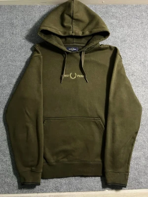 Fred Perry – Dark Green Hoodie (M) - Classic and stylish Fred Perry hoodie in dark green. Size M, length 63 cm, width 54 cm – a comfortable fit with a premium feel. The chest features the iconic Fred Perry laurel wreath embroidery, symbolizing timeless British design and quality.  ✅ Condition: Excellent – no wear, no stains 💯 Authenticity: 100% genuine, original Fred Perry branding 📦 Shipping: Dispatched immediately after purchase – fast and reliable delivery!  This hoodie combines Fred Perry’s sporty heritage with modern minimalis