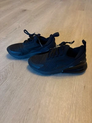 Nike Air Max 270 helsvarta sneakers - Snygga helsvarta Nike Air Max 270 sneakers med mesh-ovandel och synlig Air Max-dämpning i hälen. Skorna har sportig design, rundad tå och klassiska snörningar. 