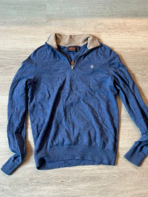 Blå halvzip Morris - Snygg blå långärmad tröja från Morris med halvzip och kontrastfärgad krage. Tröjan har ribbade muddar och en liten broderad logga på bröstet. Perfekt för en stilren och avslappnad look.