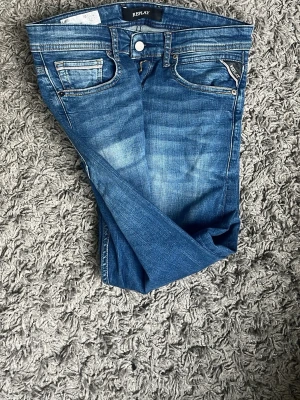 Blå jeans från Replay - Snygga blå jeans från Replay med klassisk femficksdesign och diskreta slitningar framtill. Jeansen har raka ben och detaljerade bakfickor med logotyp. Perfekta för en avslappnad och trendig look.