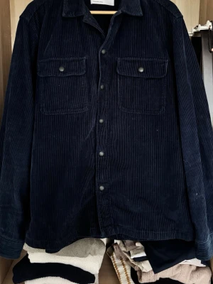 Mörkblå manchester overshirt - Stilren mörkblå overshirt från Selected Homme i mjuk manchester. Klassisk krage, två bröstfickor med lock och svarta knappar framtill. Perfekt lager-på-lager-plagg med avslappnad passform och trendig look.