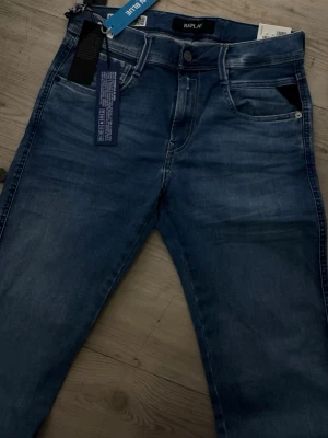 Blå slim fit jeans från Replay - Snygga blå jeans från Replay i modellen Anbass med slim fit-passform. Jeansen har klassisk femficksdesign, lätt tvättad look och är tillverkade i Hyperflex-material för extra stretch och komfort. Perfekta för en trendig och avslappnad stil.