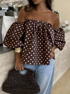 Brun offshoulder prickig blus - Trendig brun offshoulder blus med vita prickar och puffiga långa ärmar. Toppen har en lös passform och är perfekt för dig som vill sticka ut med en cool och avslappnad stil. Materialet känns lätt och luftigt.