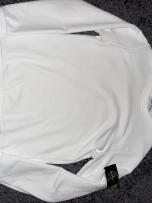 Vit sweatshirt från Stone Island - Snygg vit sweatshirt från Stone Island med klassisk rund hals och den ikoniska loggan på ärmen. Tröjan har en clean look och är tillverkad i mjukt material som känns skönt mot huden. Perfekt för en stilren och avslappnad outfit.