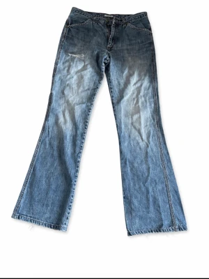 Blå bootcut jeans från Wrangler - (Pris kan diskuteras)Säljer ett par blå bootcut jeans från Wrangler med slitningar och ljus tvätt .  Tillverkade i denim med synliga sömmar och logga på bakfickan. Passar 30-32 och 30-34