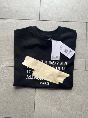 Svart Maison Margiela t-shirt - Skitsnygg svart maison margiela t shirt. Prislappen sitter kvaf och qr koden på lappen tar dig till hemsidan. Storlek M. Perfekt tröja inför sommaren med extremt skönt material. OBS fri frakt.