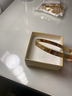 18K Guldpläterad armband - Snyggt armband i guldfärgad metall med blommönster och små glittrande stenar. Armbandet har en stilren och modern design som passar perfekt till din outfit. Levereras i en fin ask.