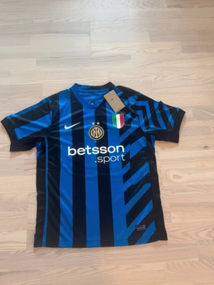 Inter Milan matchtröja Nike blå/svart - Säljer en Inter Milan matchtröja från Nike i blått och svart med diagonala ränder. Tröjan har klubbmärke, sponsorloggor och italienska mästarmärket på bröstet. Tillverkad i lätt och ventilerande material, perfekt för fotboll eller träning.