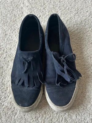 Mörkblå sneakers med fransar - Säljer ett par mörkblå sneakers i mocka med coola fransdetaljer och snörning framtill. Skorna har en vit, något tjockare sula och slip-on design. Perfekta för dig som vill ha en unik touch på dina sneakers. Passar cirka 38❤️
