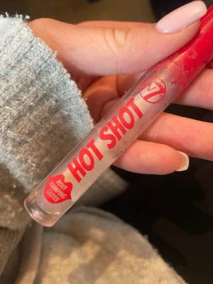 W7 Hot Shot Läppglans - W7 Hot Shot Pout Plumping Gloss är ett genomskinligt läppglans med plumping-effekt. Kommer i en smal tub med röd kork och tydlig röd text. Perfekt för dig som vill ha fylligare läppar med en glansig finish.