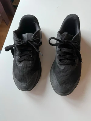 Svarta Nike sneakers i mesh - Säljer ett par helsvarta Nike sneakers med klassisk låg profil. Skorna har ovandel i mesh och syntet, snörning och diskret swoosh på sidan. Perfekta för dig som gillar stilrena och sportiga skor.