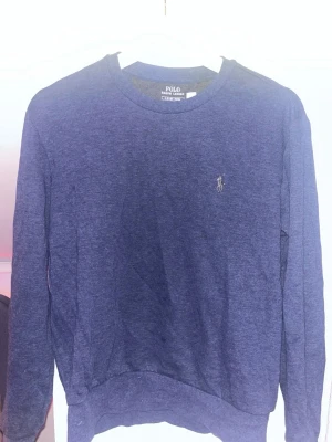 Blå sweatshirt från Polo Ralph Lauren - Mörkblå sweatshirt med rund hals och lång ärm från Polo Ralph Lauren. Diskret logga broderad på bröstet. Tröjan är tillverkad i mjukt material och har en klassisk passform som är enkel att matcha med jeans eller joggers.