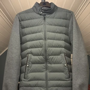 Polo Ralph Lauren Cardigan Xs - Säljer en stilren grå cardigan från Polo Ralph Lauren. Jackan har en quiltad front med dragkedja och knappar på fickorna. Ärmarna och ryggen är i ett mjukare material vilket ger en skön passform. 