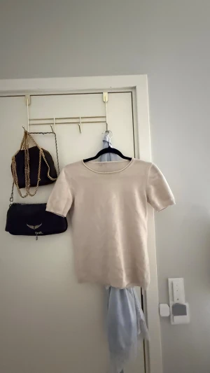 Beige Kashmir T-shirt - Säljer en stilren beige topp från Filippa K. Toppen har korta ärmar, rund halsringning och är gjord i ett mjukt material som känns skönt mot huden. Perfekt att matcha med jeans eller kjol för en clean look.