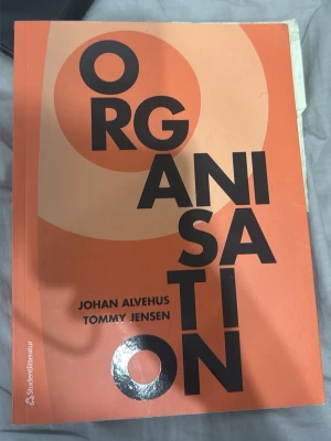 Organisation av Alvehus & Jensen - Kursbok med titeln 'Organisation' av Johan Alvehus och Tommy Jensen. Boken har ett orange och beige omslag med stora svarta bokstäver och cirkulära former. Perfekt för dig som pluggar organisation eller management.