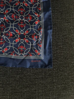 Marinblå mönstrad sjal från Gant - Snygg marinblå sjal från Gant med ett detaljerat mönster.Den är aldrig använd! Sjalen har en klassisk fyrkantig form och är tillverkad i 100% silke! Perfekt accessoar för att lyfta din outfit.