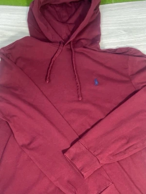Vinröd hoodie från Polo Ralph Lauren - Snygg vinröd hoodie från Polo Ralph Lauren med klassisk blå logga broderad på bröstet. Hoodien har dragsko i huvan och är tillverkad i mjukt bomullsmaterial. Perfekt för en chill och stilren look.