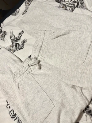 Ljusgrå mjukisbyxor med dragsko - Supersköna ljusgrå mjukisbyxor med resår i midjan och dragsko för perfekt passform. Byxorna har två sidofickor och en bakficka. Tillverkade i mjukt bomullsmaterial som känns riktigt bekvämt mot huden. Perfekta för chill dagar hemma eller när du vill vara extra comfy.