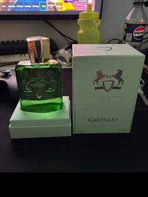 Parfums de Marly Greenley 125ml - Greenley från Parfums de Marly är en exklusiv parfym i en snygg grön glasflaska med silverdetaljer och guldfärgad kork. Flaskan har en elegant, rektangulär form och pryds av märkets ikoniska logga med två hästar. Kommer i originalkartong.