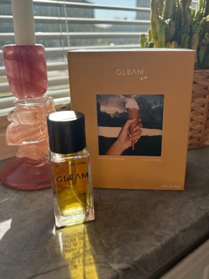 Gleam Gelatino Extrait de Parfum - Unisex parfym från Gleam i doften Gelatino. Flaskan är rektangulär i genomskinligt glas med svart lock och svart text. Förpackningen är beige med ett foto av en hand som håller en glass. Innehåller 50 ml Extrait de Parfum. Endast testad! 